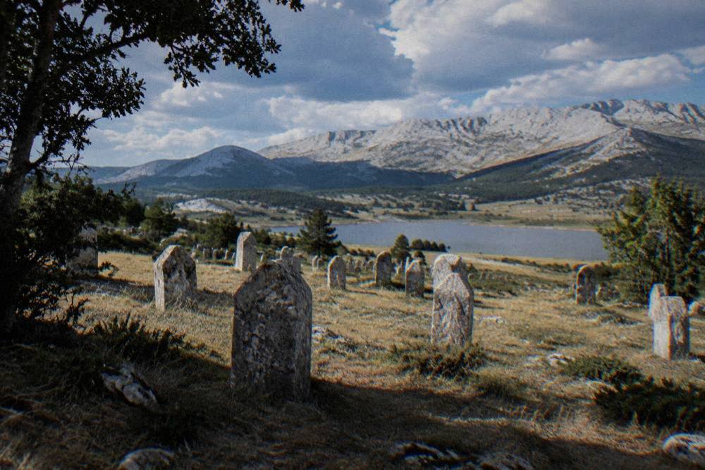 Rows of weathered medieval stone tombstones standing in open mountain grassland
