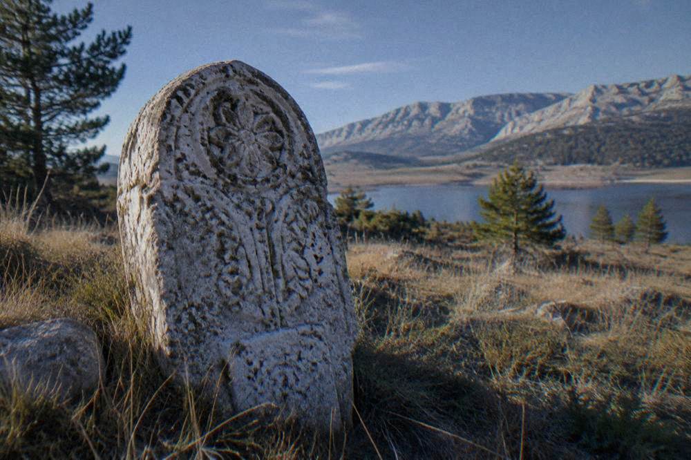 A close view of a carved limestone tombstone with worn decorative motifs in mountain grass