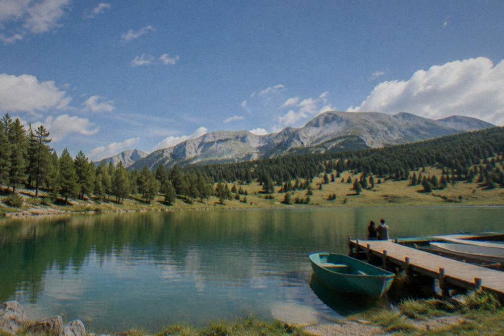 A green mountain lake surrounded by forest with small boats at a wooden jetty