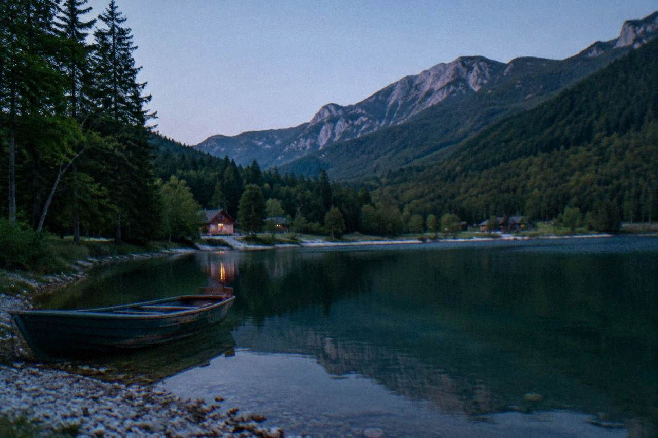 A calm green mountain lake surrounded by forested hills under a clear sky