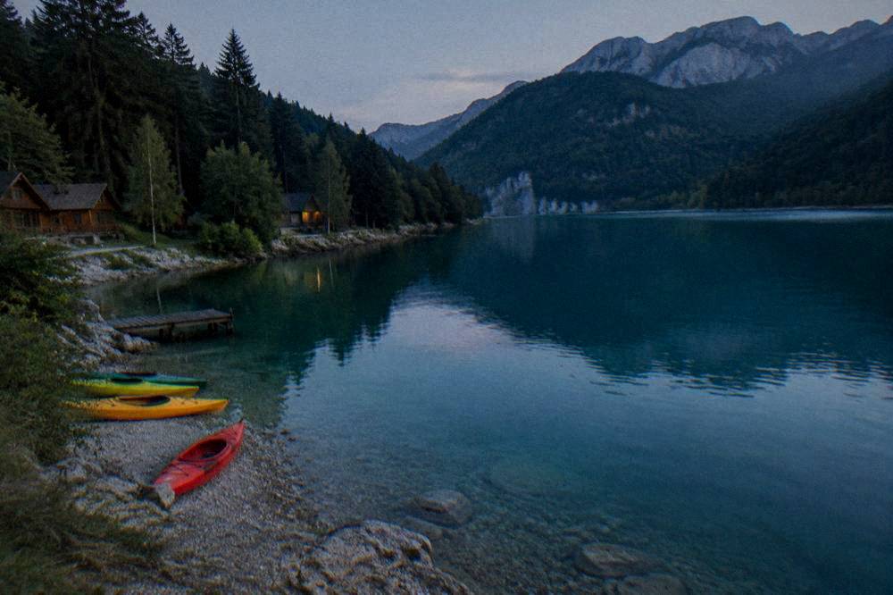 Kayaks resting on a pebble river bank beside clear turquoise water
