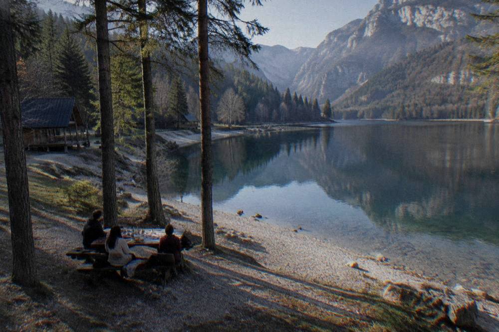 A lakeside picnic table with food and drinks under trees near the water