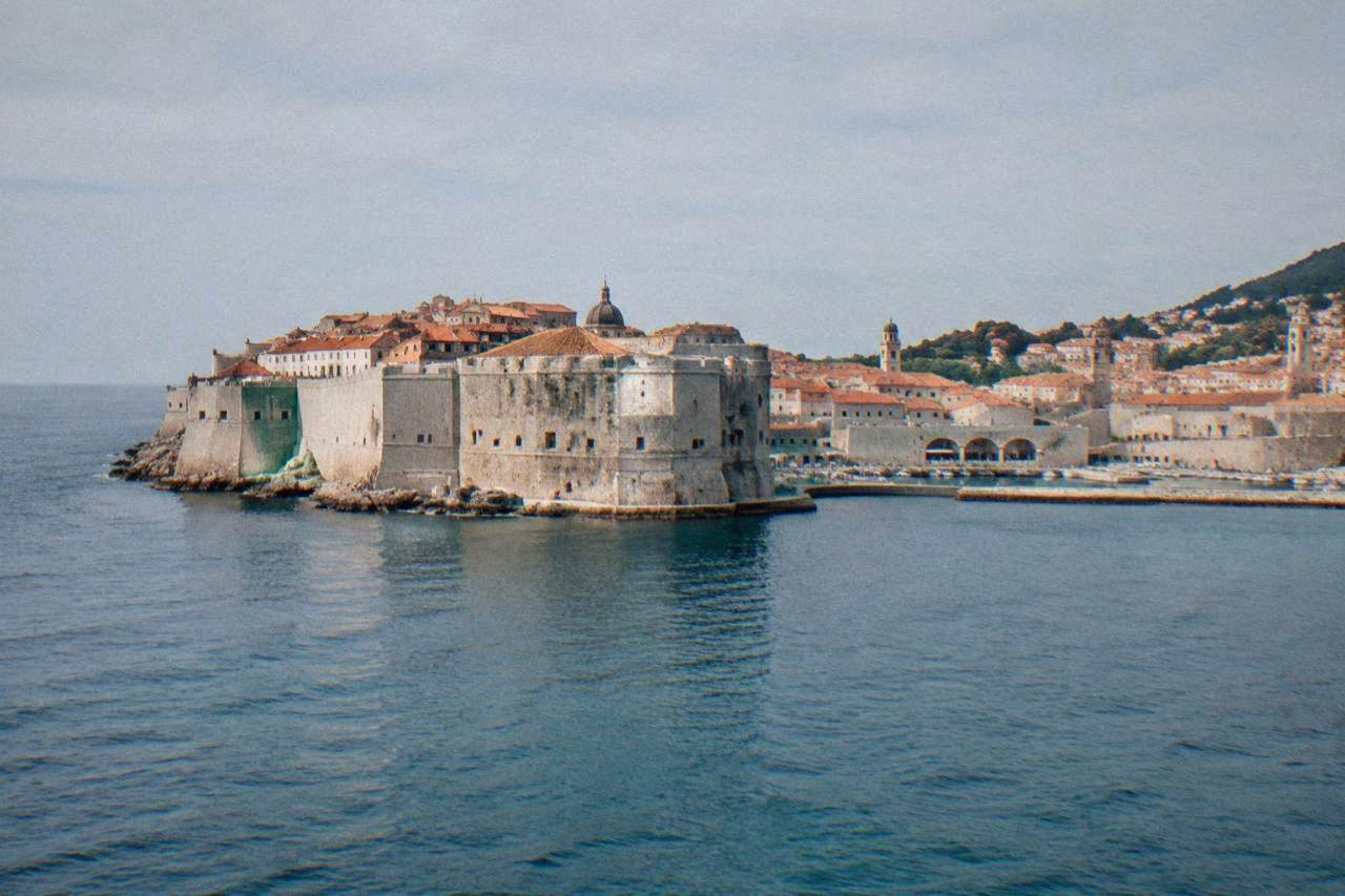The walled old town of Dubrovnik seen from the water, with terracotta rooftops and a stone wall above the sea