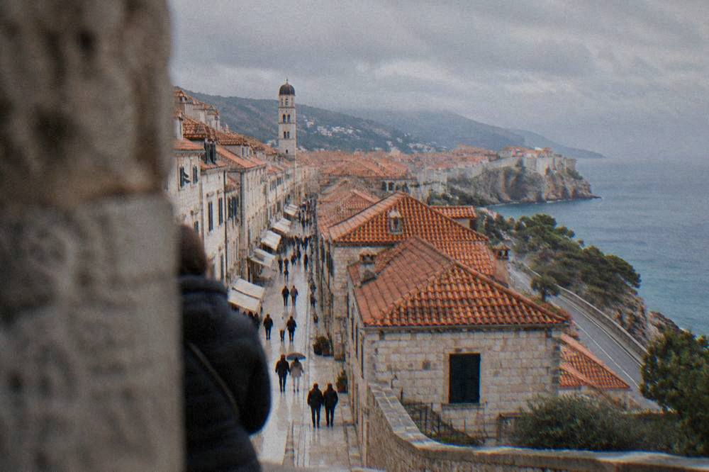 A coastal road winding above the Adriatic sea with dry hills and a distant walled town