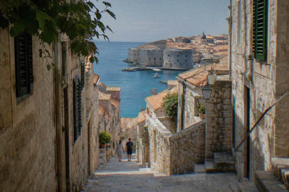 A narrow stone lane inside a walled coastal town with shutters, steps and sunlight