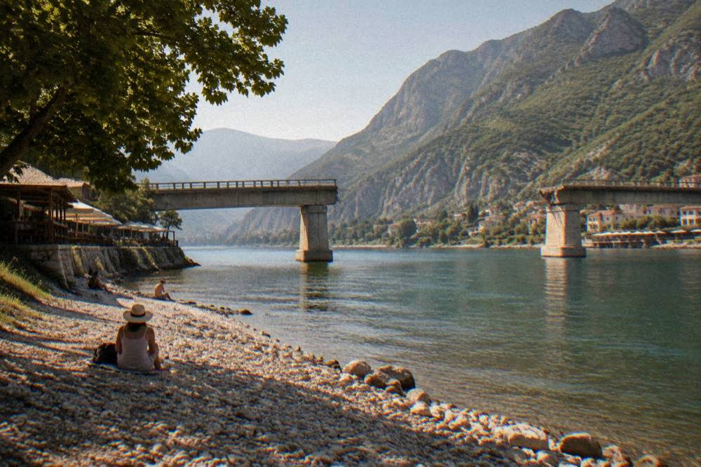 The broken bridge seen from the pebble river bank under a clear summer sky
