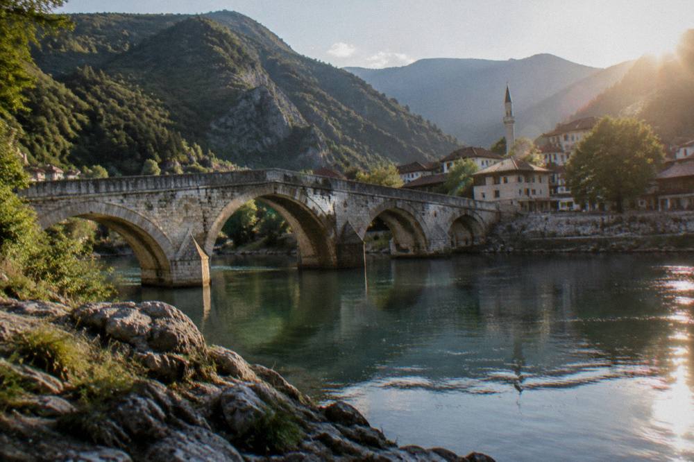 Crowd-free old stone bridge seen from a rocky riverbank in late afternoon light