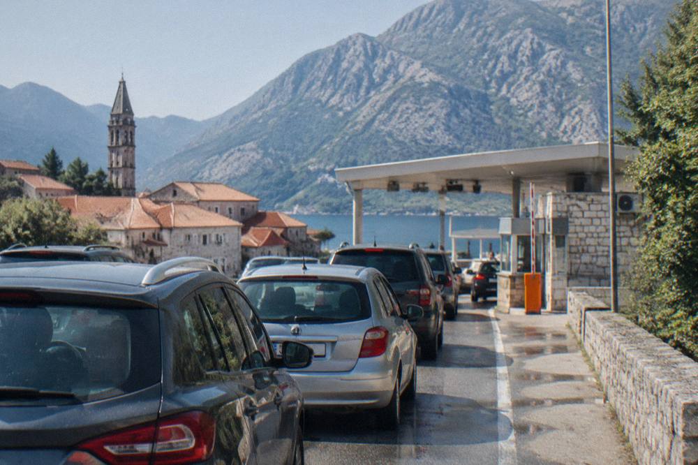 A line of cars waiting at a small border checkpoint booth in bright sunlight
