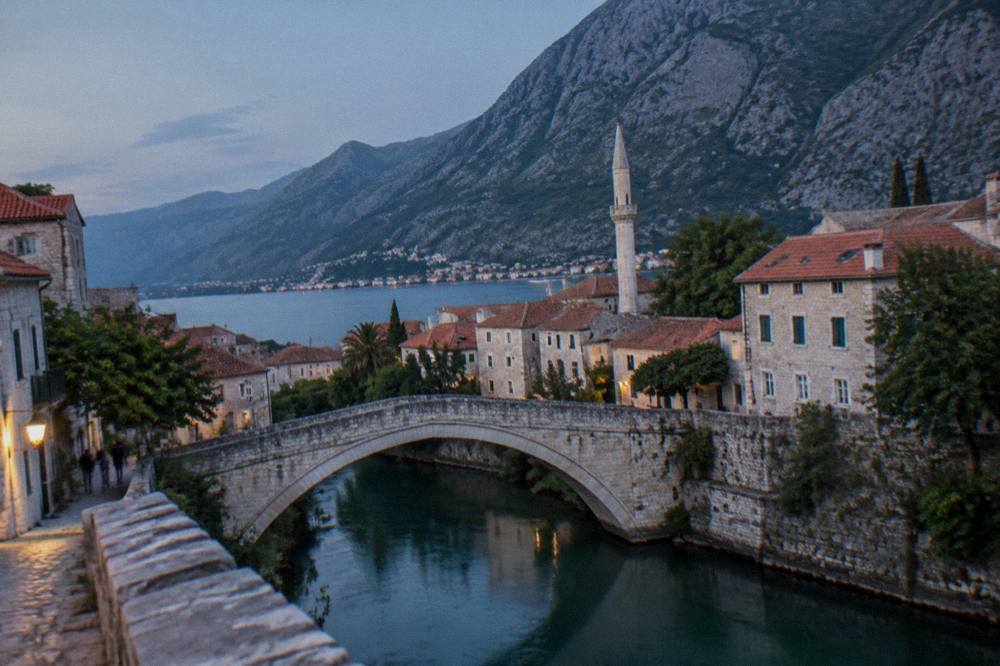 A pale stone arch bridge arching over a cold green river with a minaret behind it