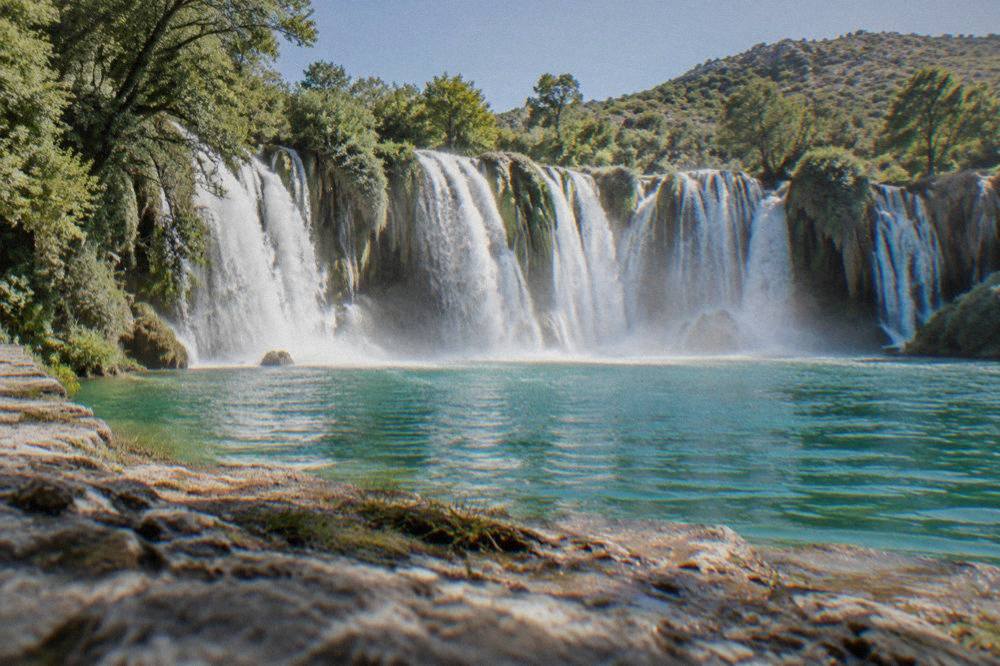 Sunlight falling on the wide arc of falling water and mist rising from the pool