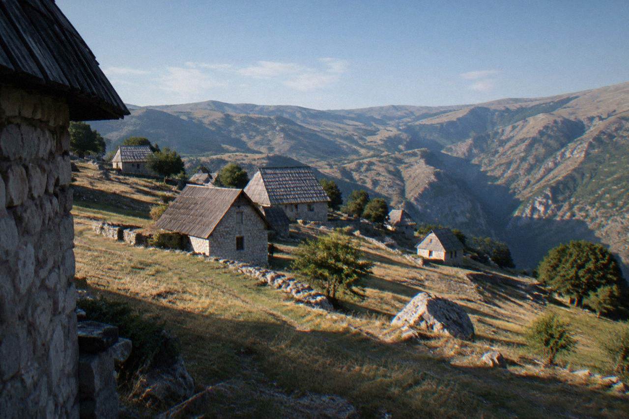 Stone houses with wooden roof shingles on a green mountain plateau under a wide sky