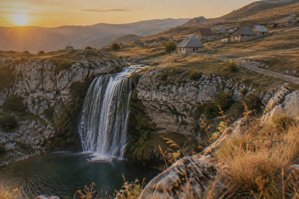 A wide green waterfall tumbling over a curved limestone cliff into a pool