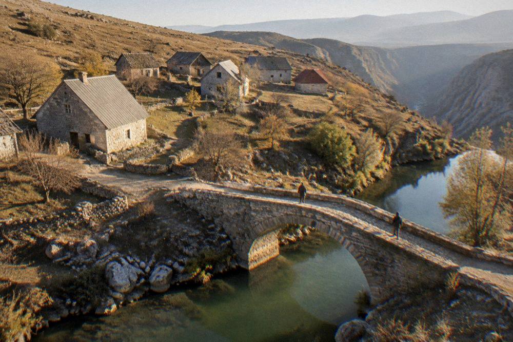An old stone bridge over a green river in a small mountain town