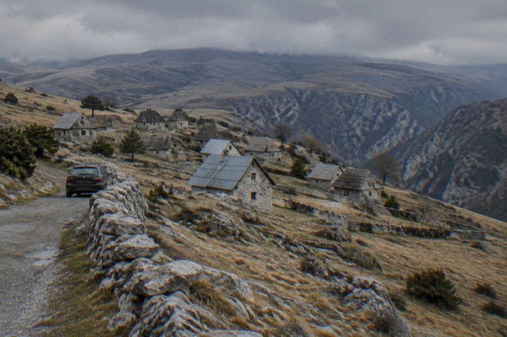 A parked car beside a stone wall on a narrow highland road with wide views