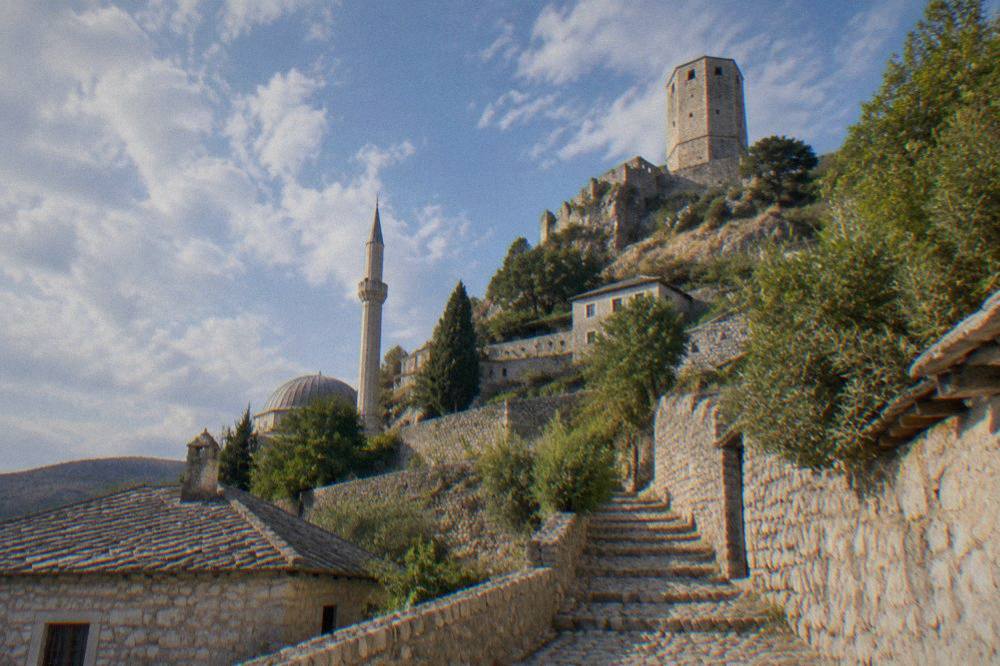 The stone watchtower of Počitelj fortress seen from the lane below, with terraced village walls