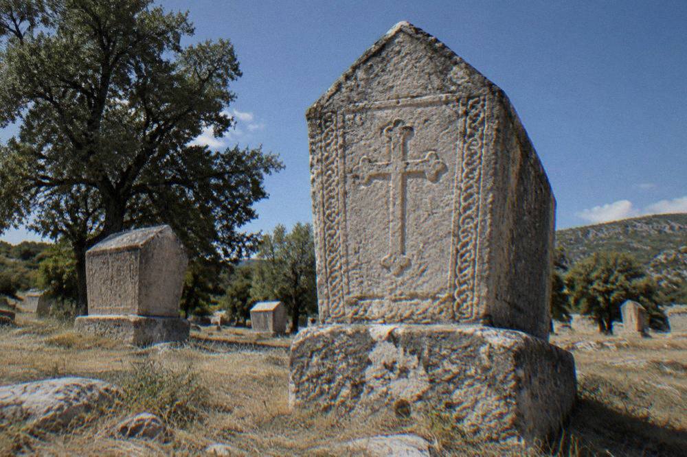 A close view of a chest-shaped stećak tombstone with a carved cross and border pattern