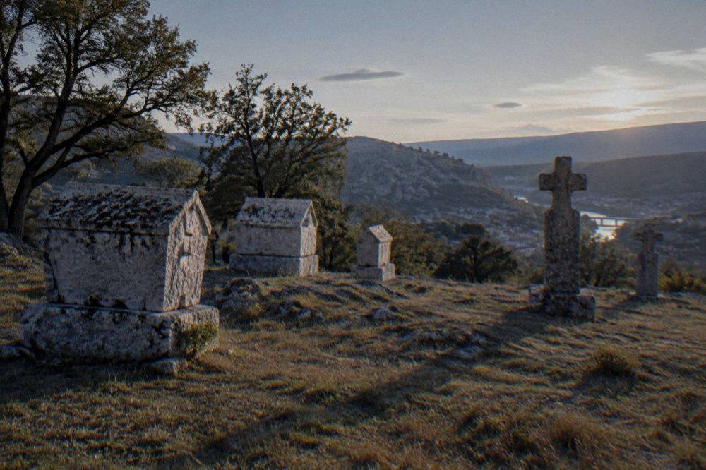 Standing crosses and chest tombstones silhouetted against an evening sky above Stolac