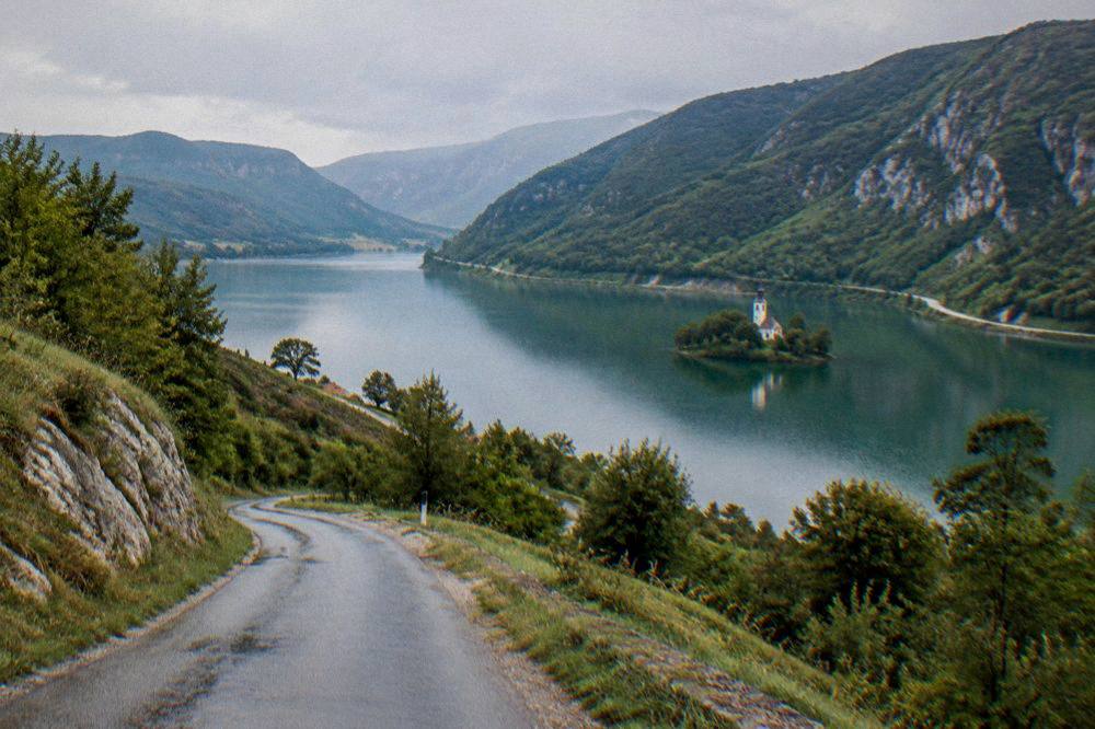 A narrow country road winding through green hills toward a lake visible in a valley below