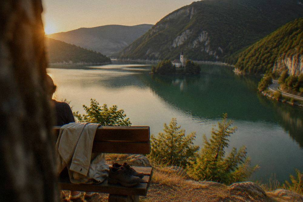 A folded light jacket and walking shoes on a wooden bench overlooking a lake