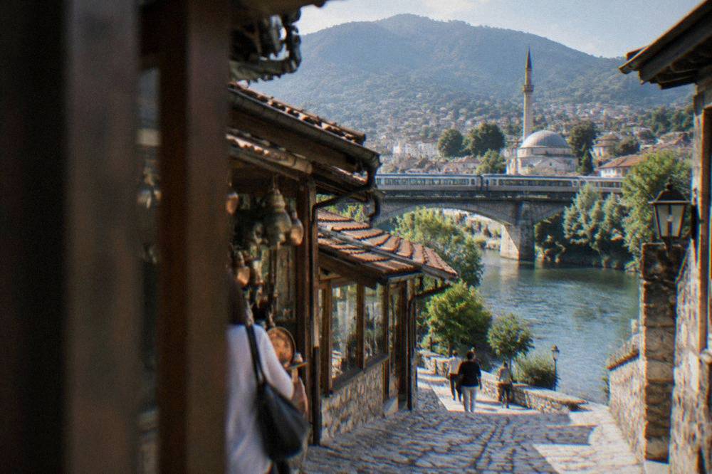 A passenger train crossing a rail bridge over the green Neretva river between hills