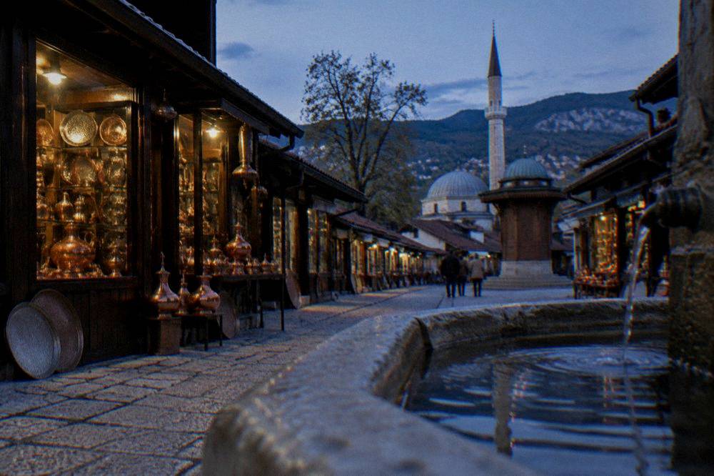 A narrow stone bazaar street with copper shops and a fountain in Sarajevo's old quarter