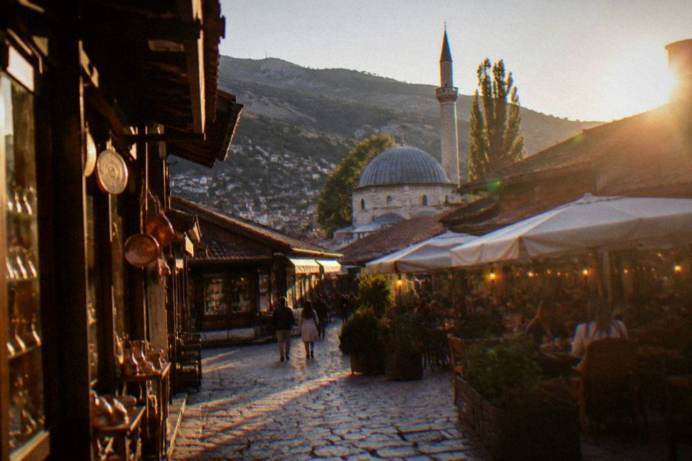 An evening street scene with lit cafe terraces and stone buildings in Sarajevo