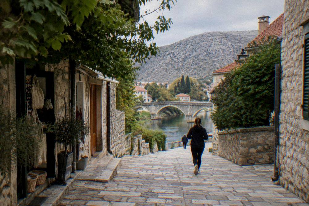 A narrow stone street with worn flagstones, small shops and green foliage overhead