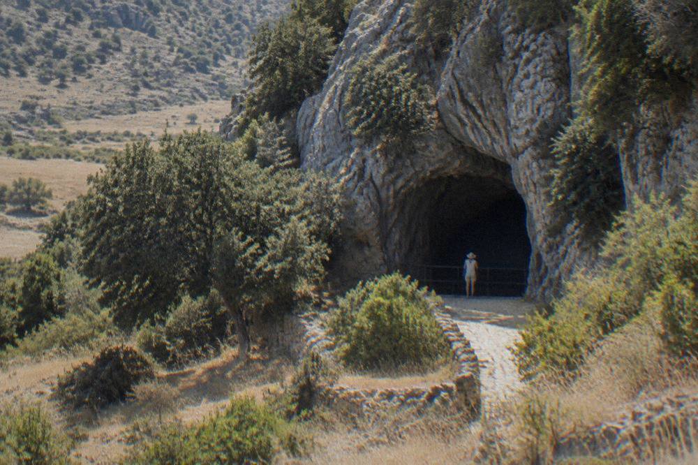 A visitor standing at the cave gate where a cold draught blows outward into the summer air