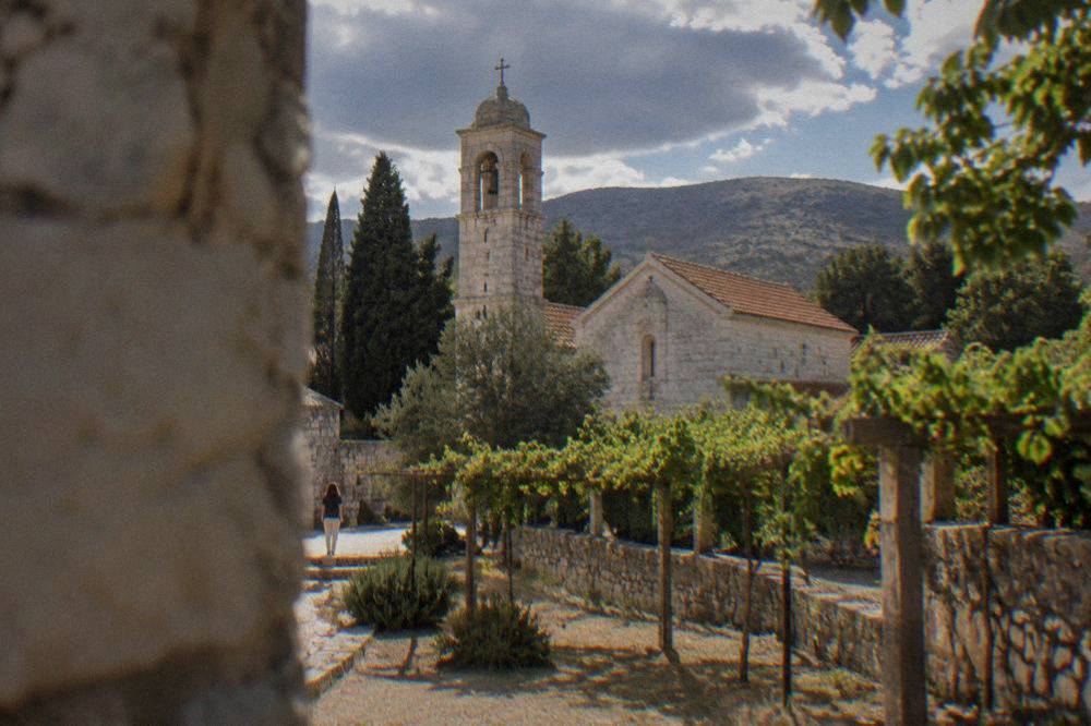 A walled monastery courtyard with a small stone church and grape vines growing along a trellis