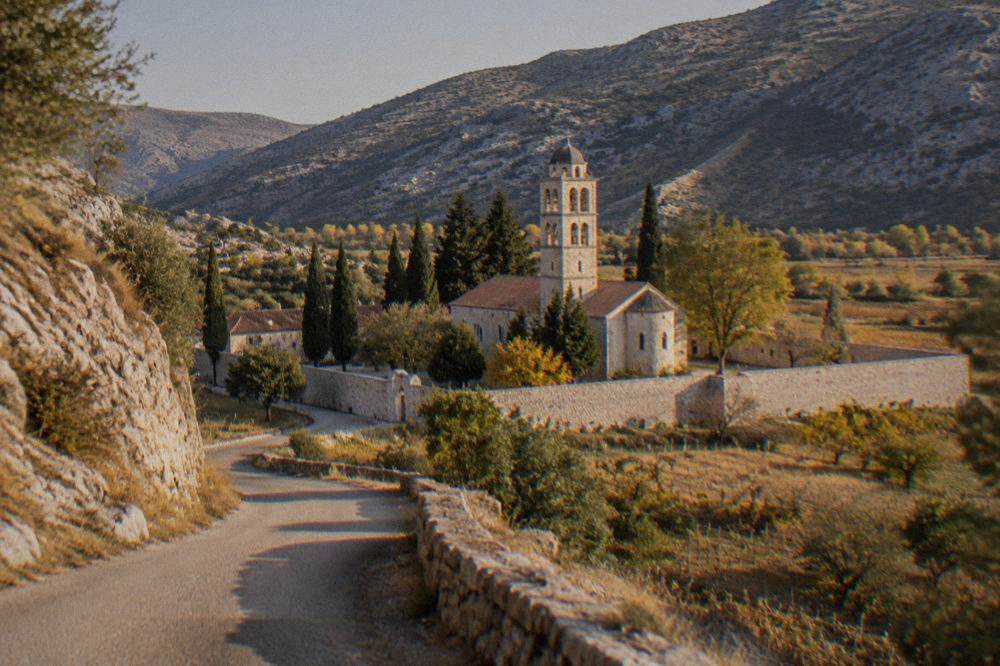 A quiet rural road winding between dry limestone hills and small vineyards in Herzegovina