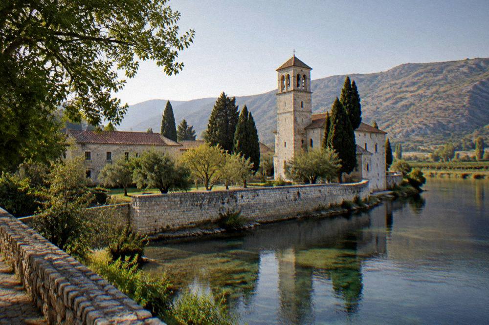 Golden late afternoon light on pale stone buildings and a river embankment in a Herzegovina town
