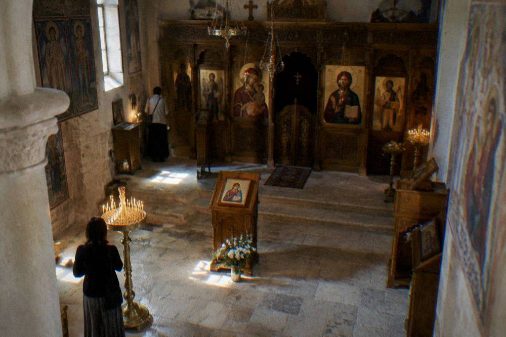 An interior view of a small Orthodox church with candle stands and painted icons in soft light