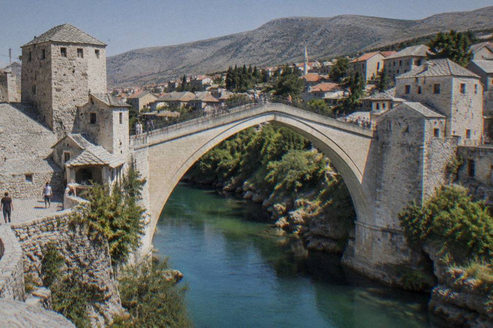 Visitors crossing the arch of Stari Most with the Neretva river and the old town rooftops below