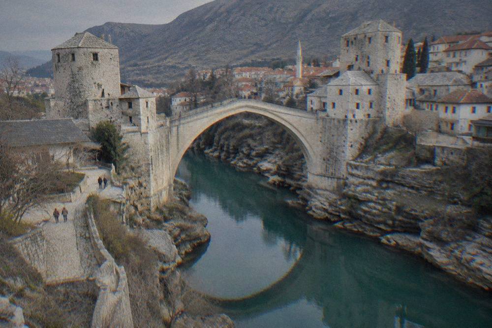 A rocky riverbank ledge below the Old Bridge with the stone arch reflected in calm green water