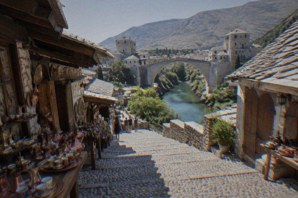 A staircase street in Mostar climbing toward a hillside bench overlooking the Old Bridge
