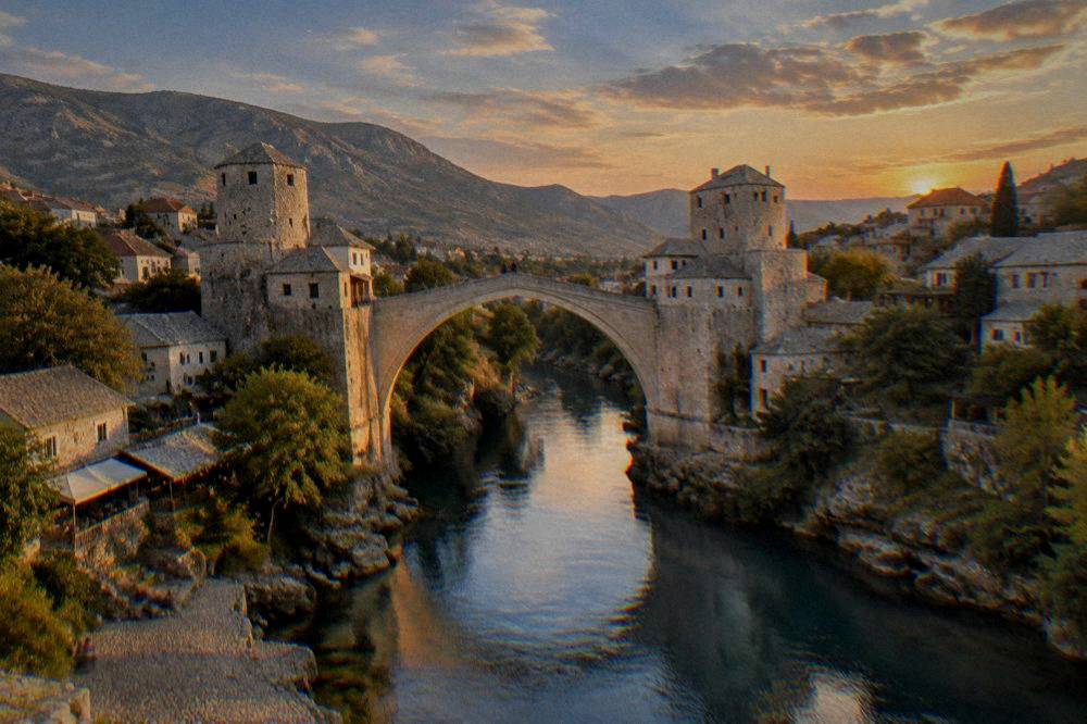 The Old Bridge silhouetted against a colourful evening sky with the Neretva reflecting blue light