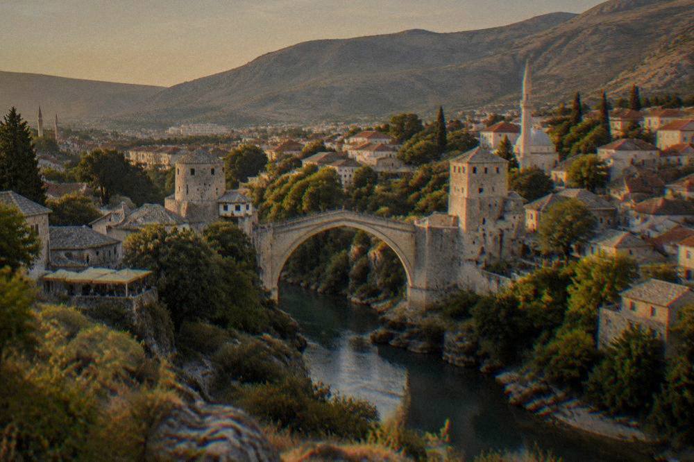 A wide panorama of Mostar from a high hillside with the Old Bridge small in the valley below
