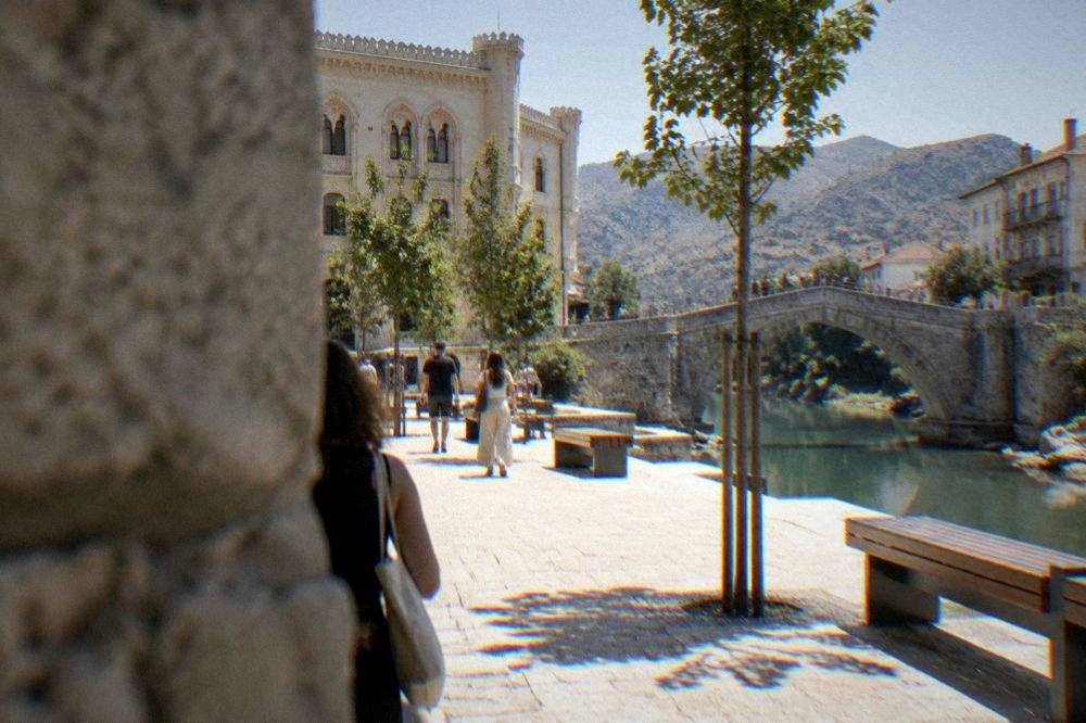 People walking across a limestone bridge arch above a calm green river