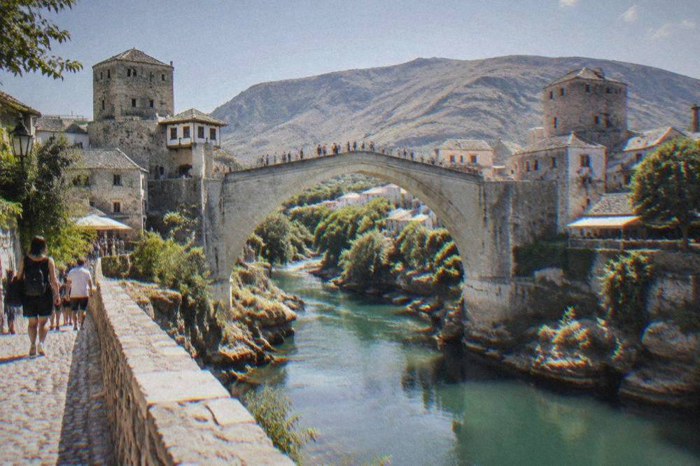 People crossing the stone arch of the Old Bridge above green river water