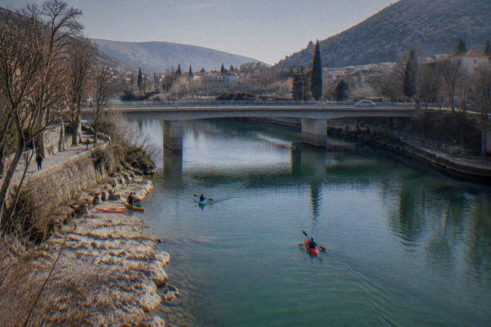 Kayaks on calm green river water beside a stony bank