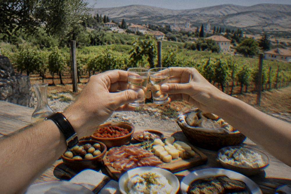 Two small glasses of rakija raised in a toast above a table of Bosnian meze dishes