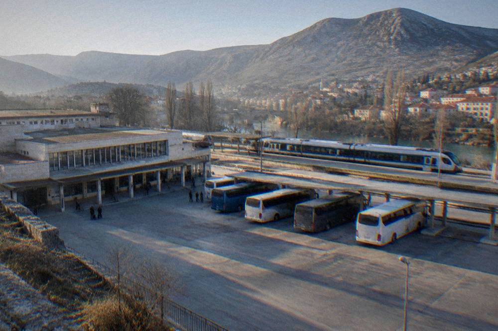 A modern passenger train standing at a station platform with mountains behind it
