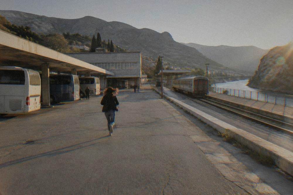 An empty two-lane road winding beside the turquoise Neretva river through a rocky valley