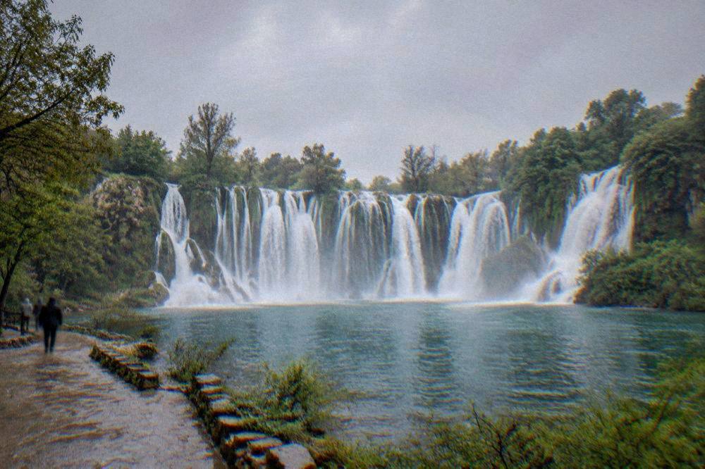 The wide curtain of Kravica waterfall falling into a green pool ringed by trees
