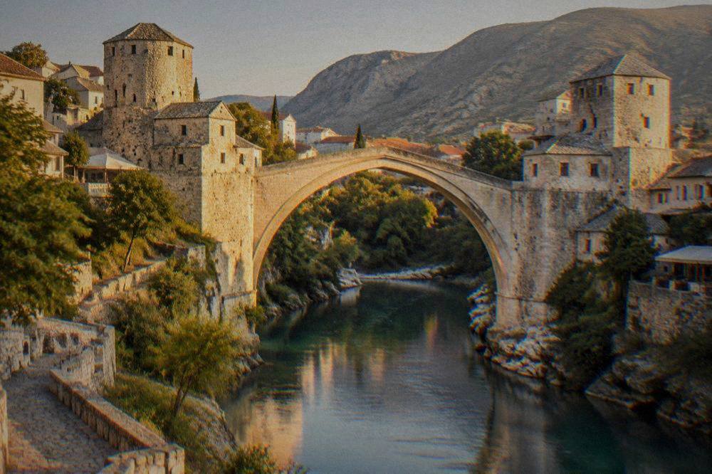The Old Bridge in Mostar lit by warm evening light with reflections in the river below