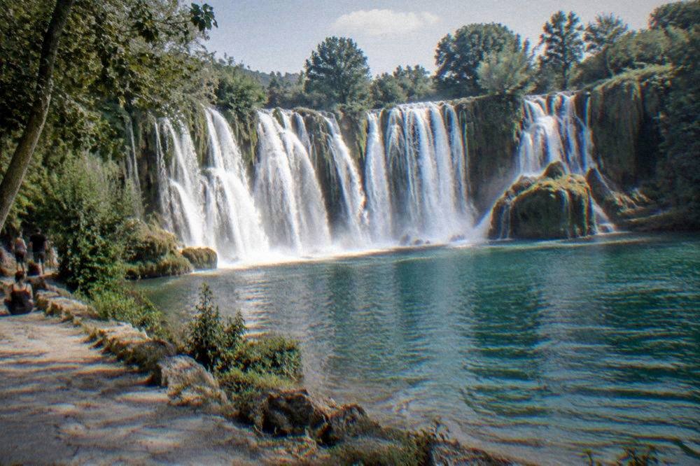 Wide waterfall curtain falling into a green pool at Kravica waterfall