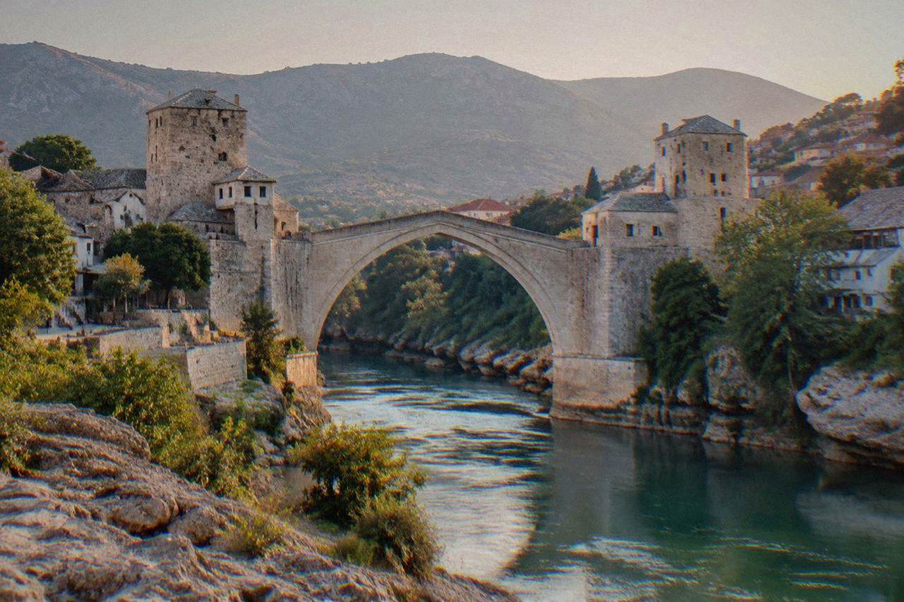 The stone arch of Stari Most seen from the rocky bank of the Neretva river at dusk
