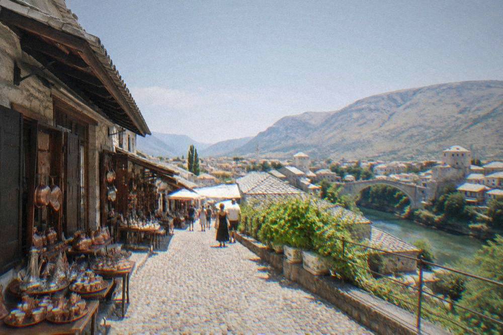 Tree-lined boulevard with cafe terraces and mid-century buildings in western Mostar