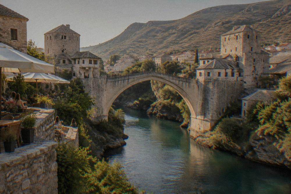 Guesthouse terraces on the east bank of the Neretva overlooking the Old Bridge at golden hour