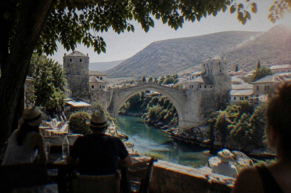 Viewers crowding the riverbank in summer watching a diver leap from the Old Bridge